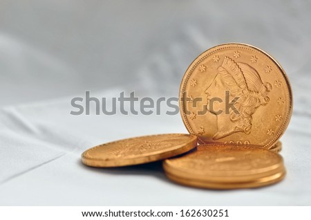 Twenty dollars golden coin standing around other four same value laying down.