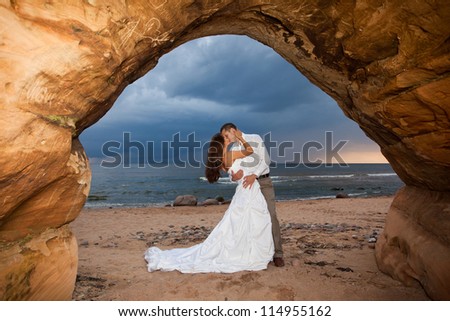 Wedding romance - bride and groom kissing in a natural rock arch with the Sea in the background.