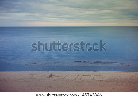 Peaceful beach with the inscription from sand: I love life, and woman sitting in the middle of the heart shape.