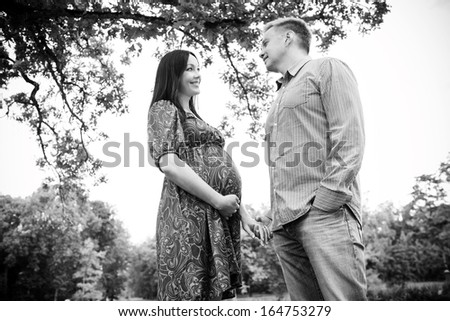 Happy pregnant woman standing by her husband and look at each other\'s eyes outdoors in the Summer. Black and white.