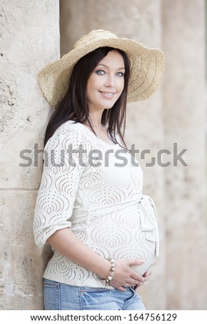 Happy pregnant woman standing outdoors in the summer from the side and looking at camera.