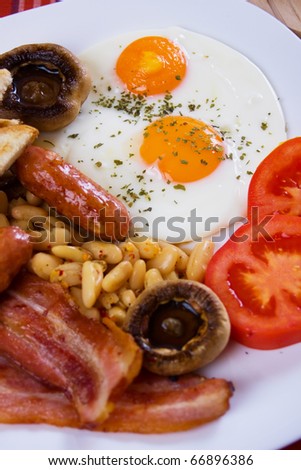 Traditional english breakfast food, fried eggs, bacon, sausage and beans (focus on egg)