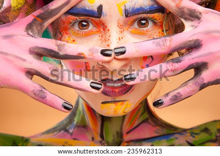 Beautiful fashion woman with bright color face art and body art. Paint on face. Posing in studio. Creative portrait on yellow background.