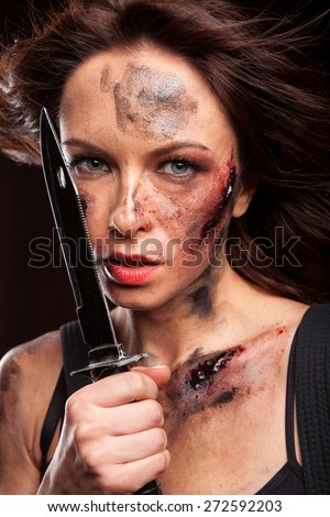 Woman holding a sharp knife with blood drops on face. Riot girl in leather jacket.
