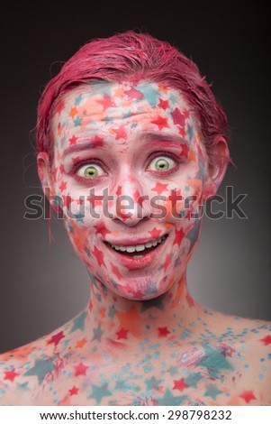 Emotional portrait of a surprised young woman with stars on the face and painted hair in pink