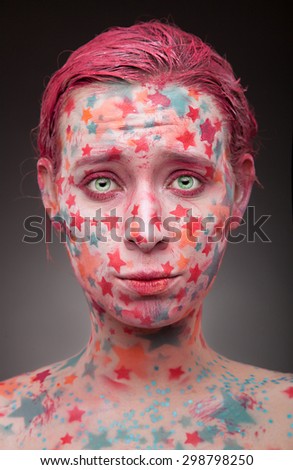 Emotional portrait of a sad young woman with stars on the face and painted hair in pink  looking like a fabulous creature in studion on grey background