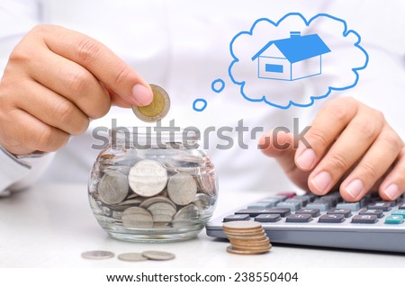 businessman hand putting money coins into glass piggy bank for buy home