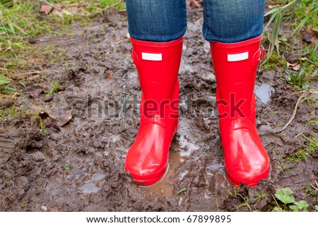 Bright shining clean red rain boots on a girl while she stands in the mud puddle.