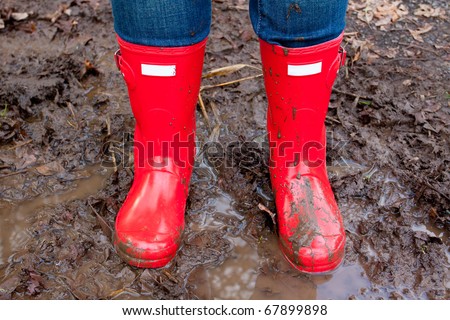 Red rain boots on the legs of a girl after she played in the mud and got them dirty and muddy.