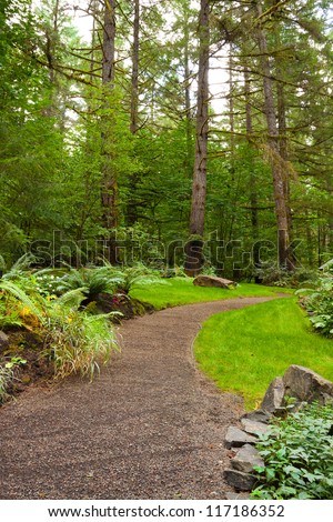 A beautiful path leads into a perfectly manicured garden at an Oregon wedding venue location. There is green, trees, plants, and stone in this vertical image.