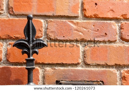 A wrought iron metal gate with a fleur de lis pattern at the top is constructed up against a brick wall at a wealthy estate.
