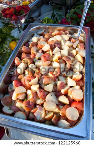 A serving dish of cooked potatoes and a serving spoon in the buffet line of a wedding reception. The meal looks healthy and delicious.