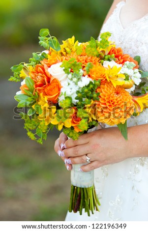 A bride in her white wedding dress holds her bouquet of orange, green, and yellow flowers on her wedding day.