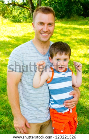 A father has his arm around his son outdoors.