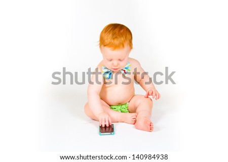 A one year old boy plays with a cell phone in the studio with a white background.