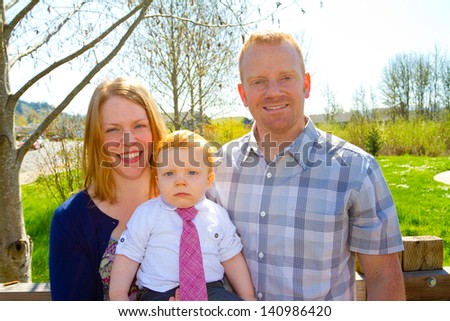 A man and a woman hold their baby one year old son while posing for a family photo outdoors.