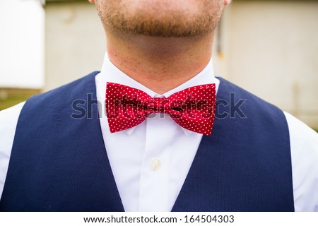 A fashionable groom wears a red and white bowtie with a navy blue vest on his wedding day.
