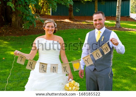 A bride and groom hold a banner of burlap that reads thank you so they can use it later for their thank you cards.