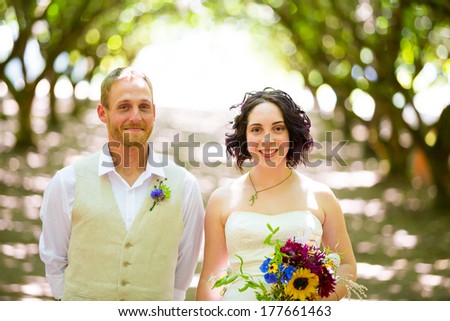 Bride and groom pose for a portrait in a backlit orchard on their wedding day in Oregon with light filtering through the trees.