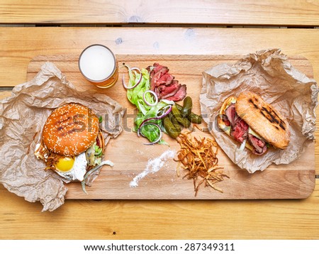 Burgers with onion, chips, pickles, lettuce, bacon and beer on a wooden board