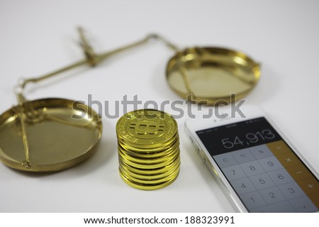 Bit-coin counting concept with a neat stack of gold Bit-coins alongside a tablet or mobile and a vintage brass pendulum pan scale for weighing