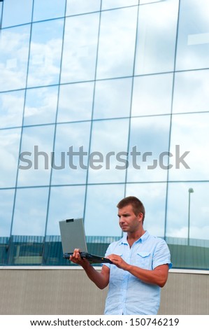 Business man with laptop in front of modern business building.