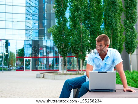 Business man with laptop in front of modern business building.