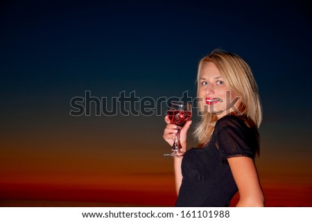 beautiful lady i black dress with glass of wine on the beach