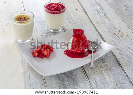 two glasses of panna cotta with caramelized and red sauce topping and a plate with panna cotta and strawberry decoration on a wooden table