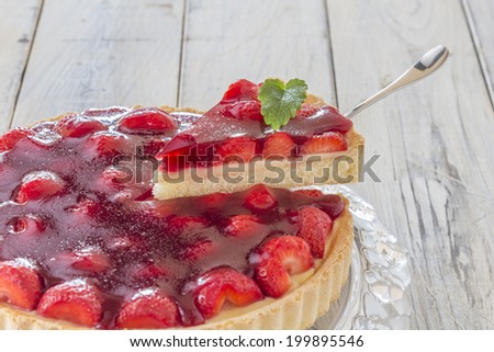 Homemade strawberry cake with one slice lifted up on a glass platter on a wooden table