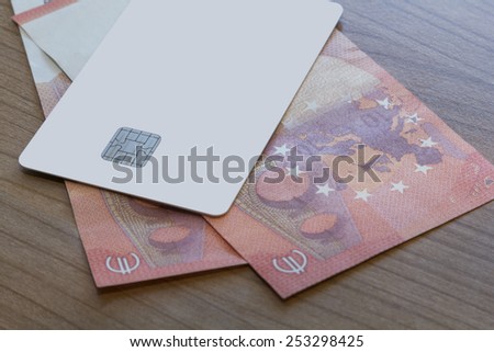 A Blank white Credit or Debit Card on two 10 Euro notes on a wooden table