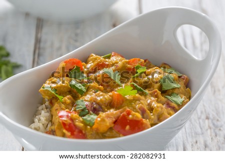 chicken curry, red pepper and coriander leaves with rice in a white bowl