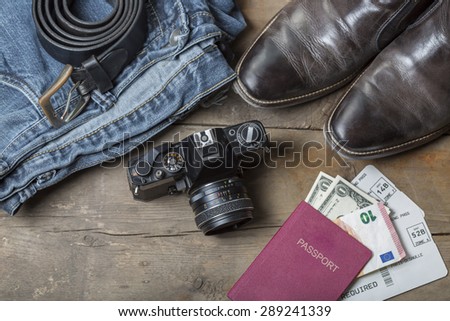 Jeans, Belt, leather boots, vintage camera and passport with tickets and money on a rustic wooden background