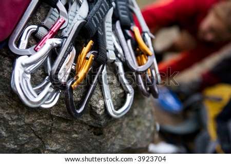 A pile of quick draw carabiners with climbers out of focus in the background.
