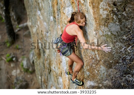 An eager female climber on a steep rock face looks for the next hold - viewed from above.  Shallow depth of field is used to isolated the climber with the focus on the head.