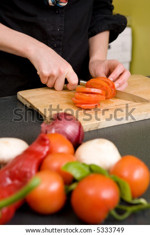 A detail image of a woman slicing tomatoes on a cutting board at home. - shallow depth of field with the focus on the tomato and knife