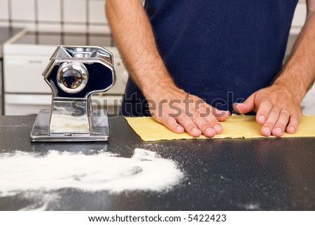 A Male making pasta on the counter in the kitchen.