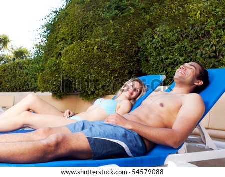 A couple suntanning on beach chairs beside a pool
