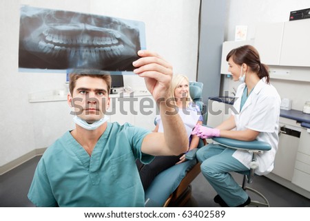 Radiodentist checking x-ray with assistant and patient having conversation in the background