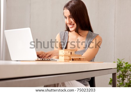 A creative professional woman working at a desk with a laptop and house model