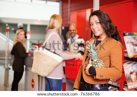 Portrait of a customer carrying pineapple in supermarket with people in the background