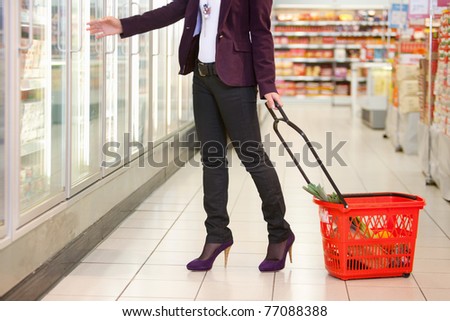 Low section of woman in front of refrigerator carrying basket in the supermarket