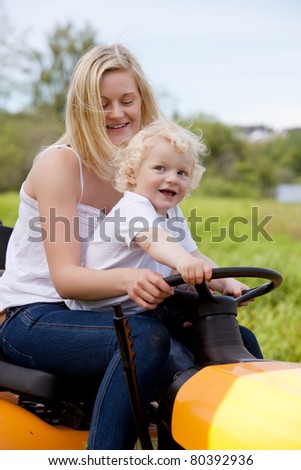 A mother driving a lawn mower tractor with happy smiling son