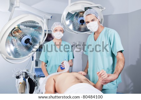 Female doctor applying gas and male doctor checking pulse rate of patient