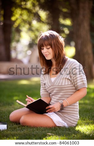 Pretty brunette student writing in a journal on a university campus