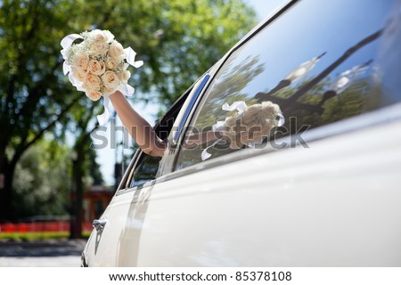 Bride waving hand from car holding flower bouquet