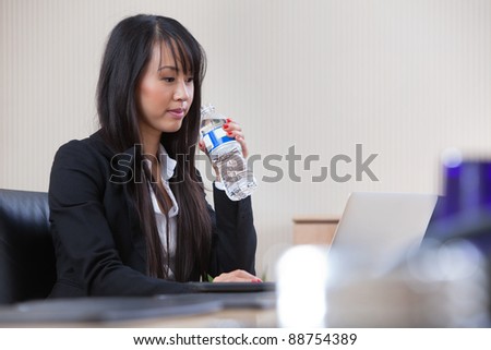 Young beautiful businesswoman drinking water at work