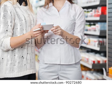Mid-section of female pharmacist advising customer how to take medicine