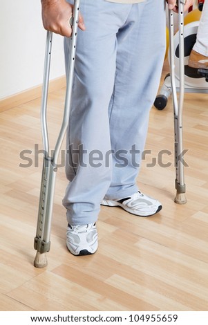Low section of a woman standing with crutches on a wooden floor