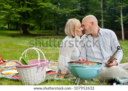 Romantic couple on picnic with food on portable barbecue in forest park